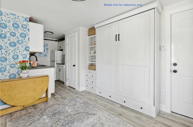 interior space featuring dark stone counters, light wood-type flooring, a sink, and white cabinetry