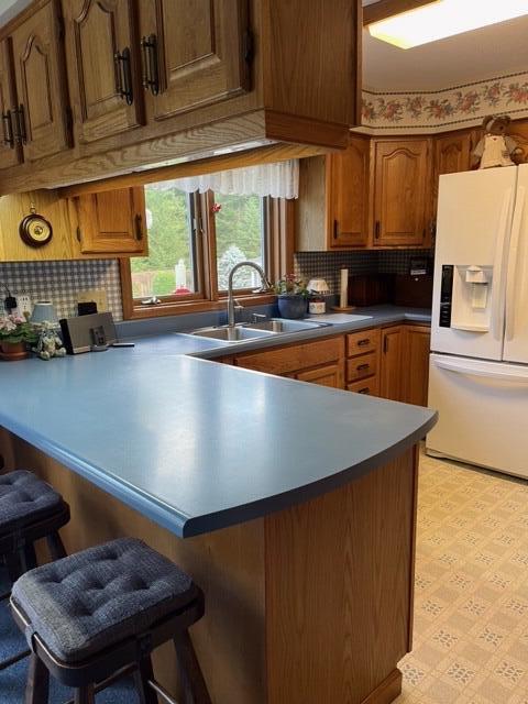 kitchen with white refrigerator with ice dispenser, a kitchen breakfast bar, backsplash, sink, and light tile patterned flooring