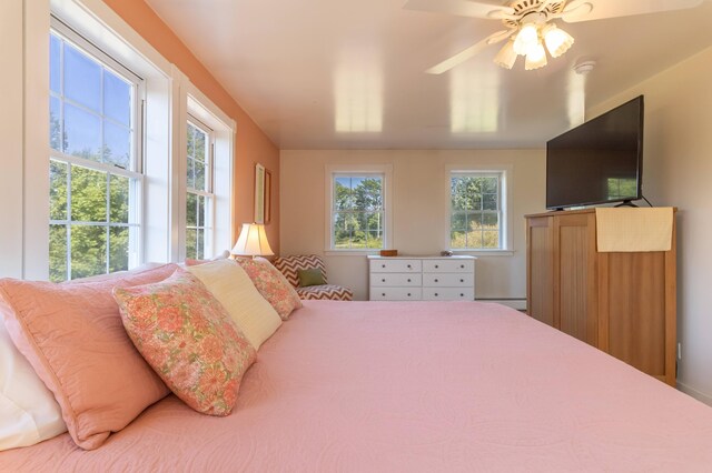 bedroom featuring ceiling fan, a baseboard heating unit, and multiple windows