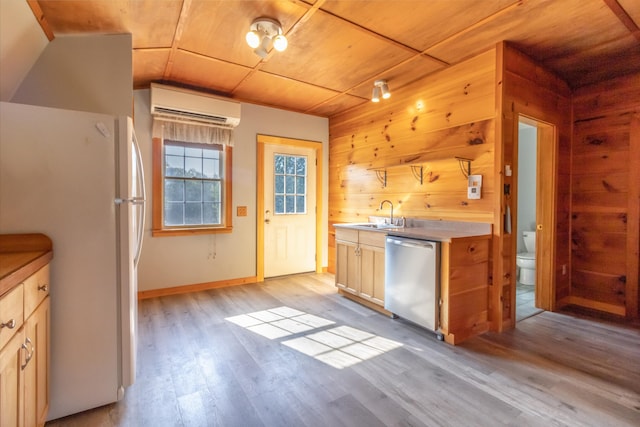kitchen with a wall mounted AC, wood walls, light wood-style flooring, stainless steel dishwasher, and freestanding refrigerator