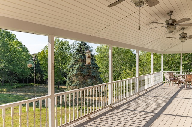 wooden deck featuring outdoor dining area, ceiling fan, and a yard