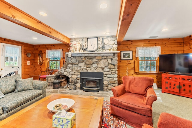 living room with a fireplace, wood walls, a wood stove, carpet flooring, and beam ceiling