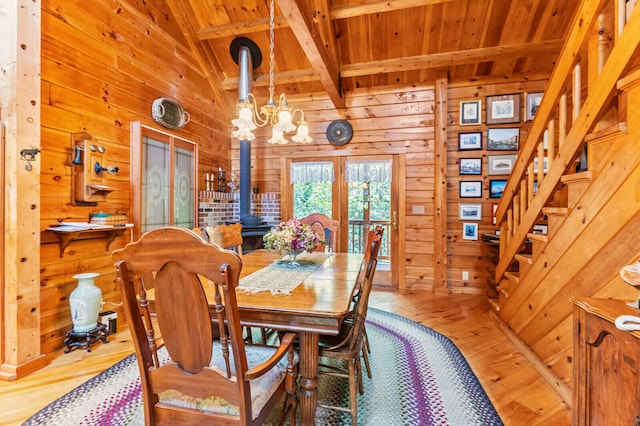 dining space with a wood stove, wood-type flooring, french doors, a chandelier, and wooden walls