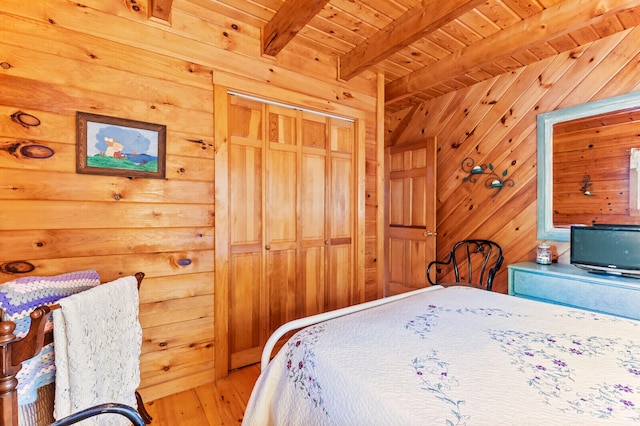 bedroom featuring wood walls, beamed ceiling, wooden ceiling, a closet, and hardwood / wood-style flooring