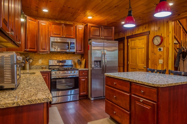 kitchen with light stone counters, wood walls, decorative light fixtures, appliances with stainless steel finishes, and dark hardwood / wood-style floors