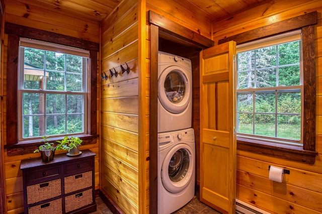 clothes washing area featuring stacked washer / drying machine, wooden walls, a baseboard heating unit, and wooden ceiling