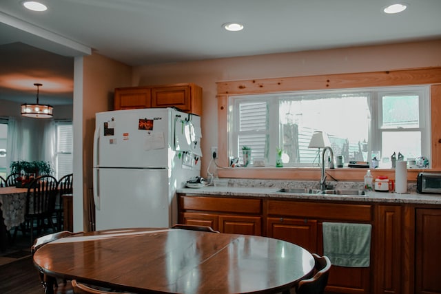 kitchen featuring light stone counters, pendant lighting, sink, and white fridge