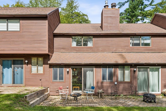 back of house with a shingled roof, a chimney, a patio area, and a fire pit