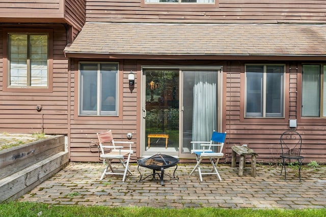 back of property with a fire pit, a shingled roof, and a patio area