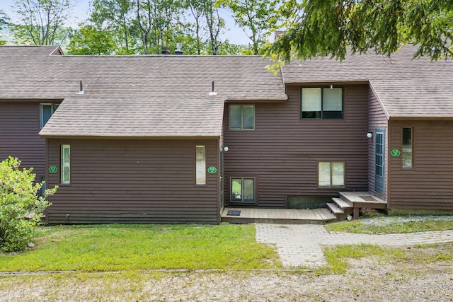 back of property featuring a deck, roof with shingles, and a lawn