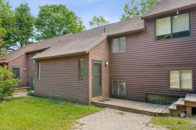 rear view of house with a shingled roof, a lawn, and a deck