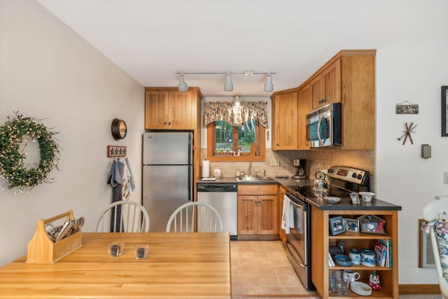 kitchen with decorative backsplash, dark countertops, brown cabinets, stainless steel appliances, and a sink