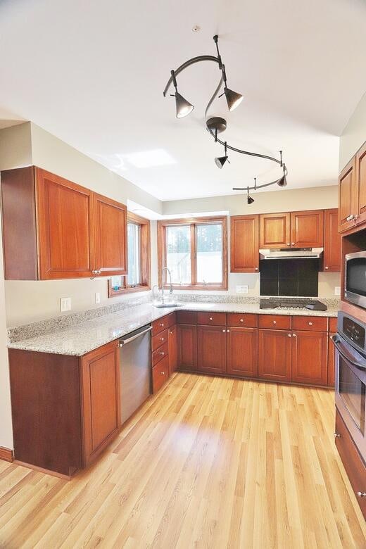 kitchen featuring appliances with stainless steel finishes, light hardwood / wood-style flooring, light stone countertops, and sink