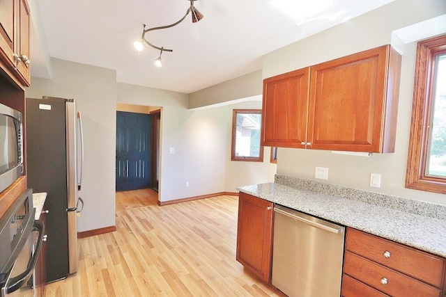 kitchen with light stone countertops, appliances with stainless steel finishes, and light hardwood / wood-style floors