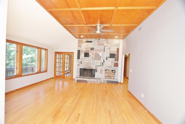 unfurnished living room featuring ceiling fan, wood-type flooring, wooden ceiling, a stone fireplace, and french doors