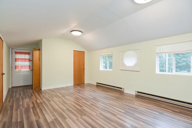 additional living space with a healthy amount of sunlight, a baseboard heating unit, hardwood / wood-style flooring, and vaulted ceiling