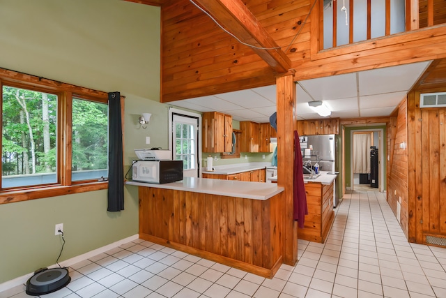 kitchen with a wealth of natural light, kitchen peninsula, light tile patterned floors, and wooden walls