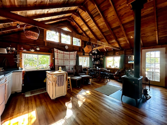 unfurnished living room featuring wood-type flooring, vaulted ceiling with beams, a wood stove, and a healthy amount of sunlight