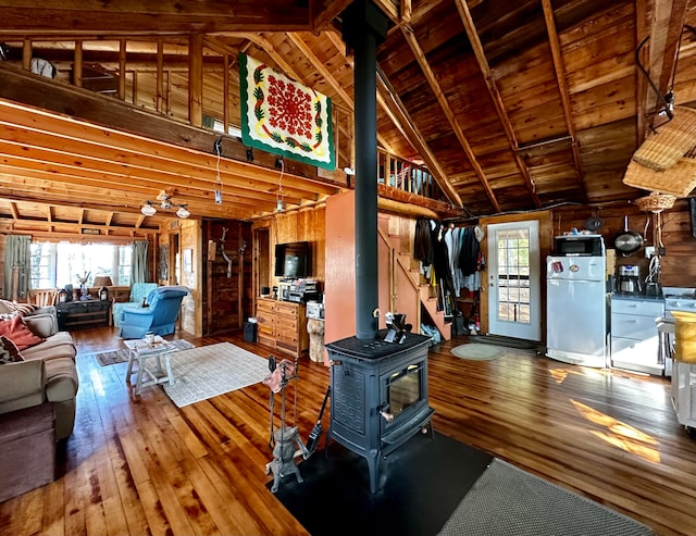 living room with lofted ceiling with beams, wood ceiling, hardwood / wood-style flooring, a wood stove, and wooden walls