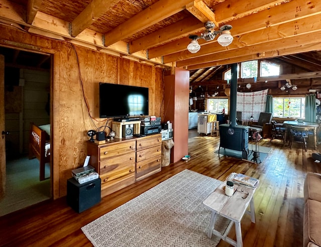 living room featuring wood-type flooring, beamed ceiling, wood walls, and a wood stove