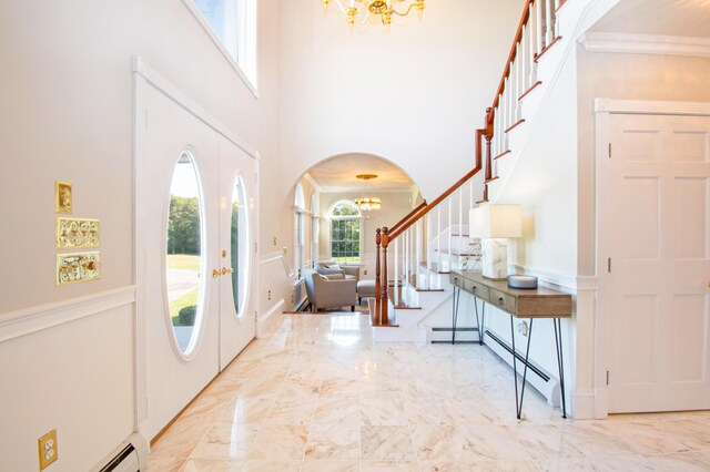 foyer entrance featuring a baseboard heating unit, a high ceiling, ornamental molding, and an inviting chandelier