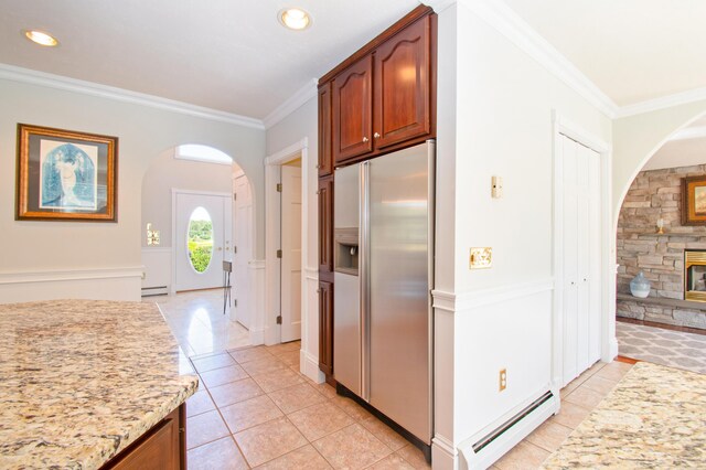 kitchen featuring a baseboard heating unit, light stone counters, stainless steel fridge, a stone fireplace, and ornamental molding