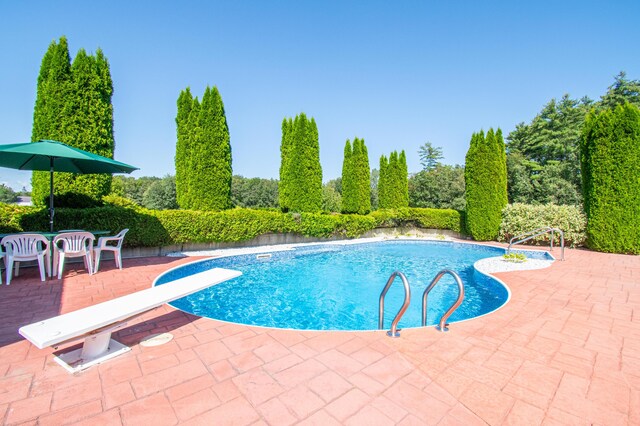 view of swimming pool with a diving board and a patio