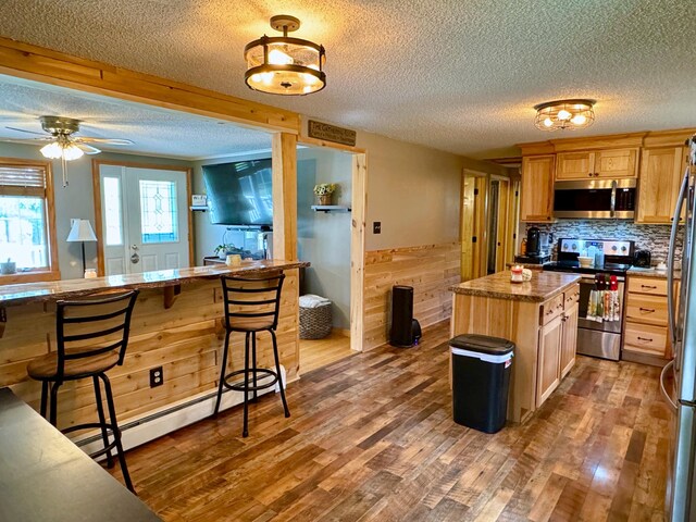 kitchen with a textured ceiling, wood-type flooring, a kitchen bar, stainless steel appliances, and baseboard heating