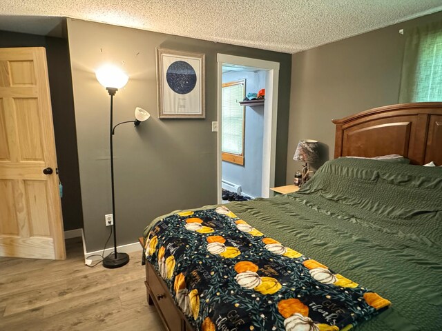 bedroom with baseboard heating, baseboards, light wood-style floors, and a textured ceiling