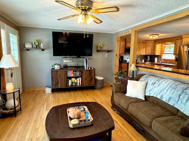 living room featuring light wood-style flooring, ceiling fan, ornamental molding, and a textured ceiling