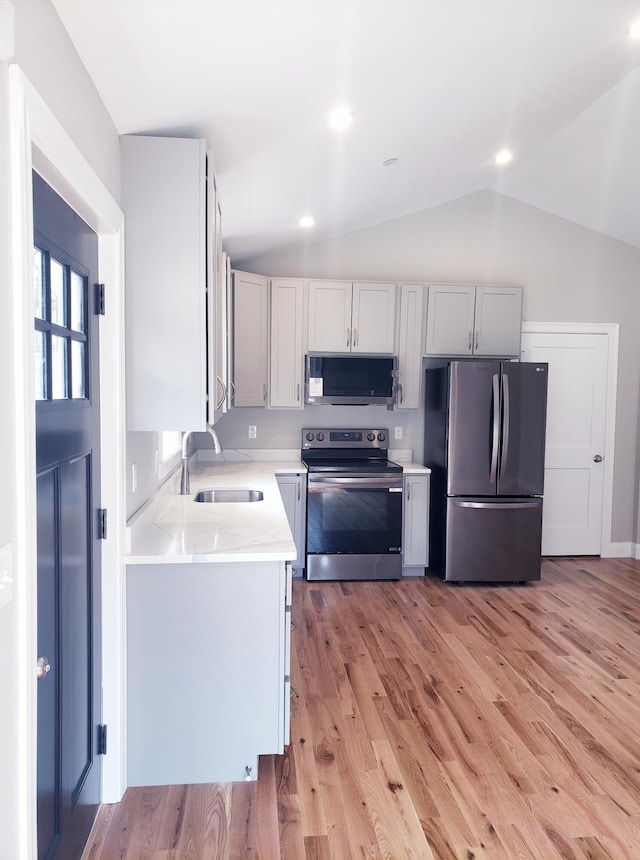 kitchen with lofted ceiling, stainless steel appliances, light hardwood / wood-style floors, and sink