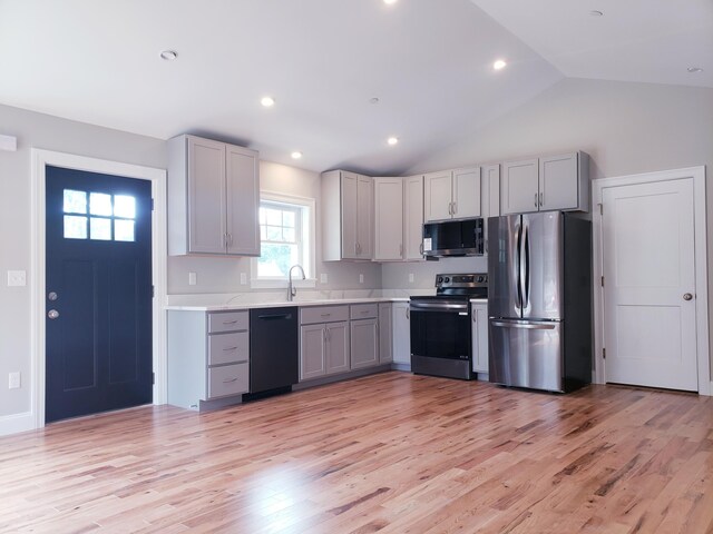 kitchen with light wood-type flooring, vaulted ceiling, gray cabinetry, and appliances with stainless steel finishes