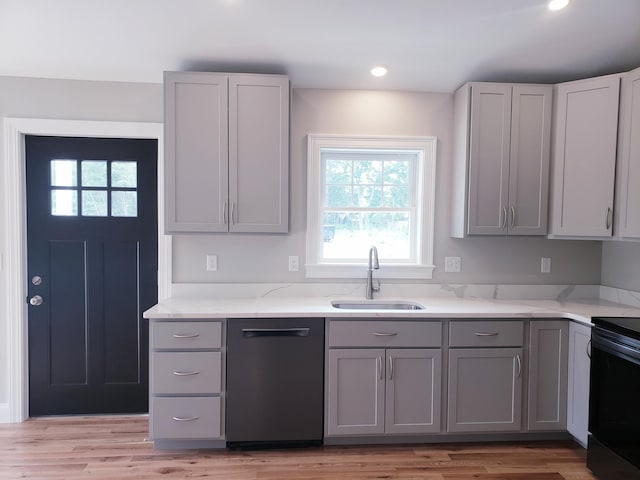 kitchen with black appliances, light stone counters, sink, and light hardwood / wood-style flooring