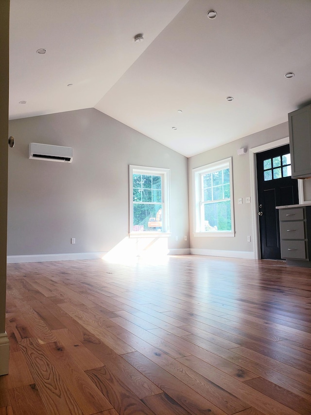 unfurnished living room featuring lofted ceiling, a wall mounted AC, and wood-type flooring