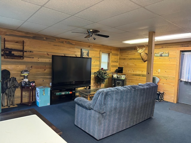 living room with a paneled ceiling, ceiling fan, and wooden walls