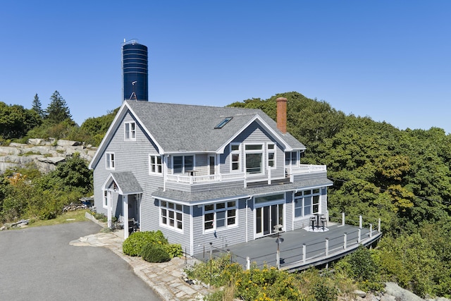 rear view of house featuring a balcony, a shingled roof, and a chimney