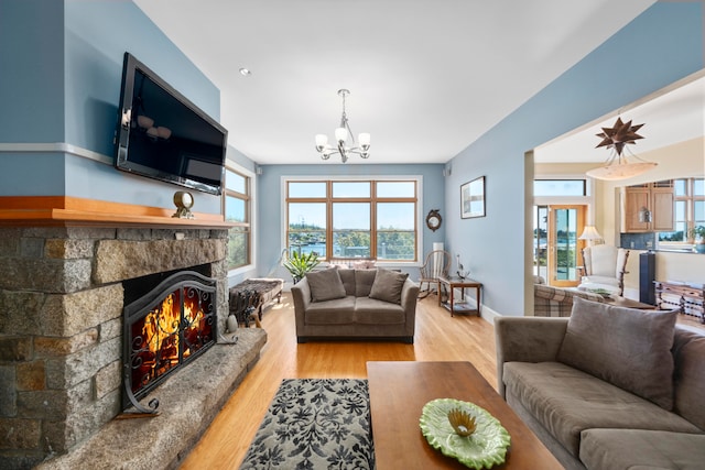 living room featuring light wood-type flooring, plenty of natural light, a notable chandelier, and a stone fireplace