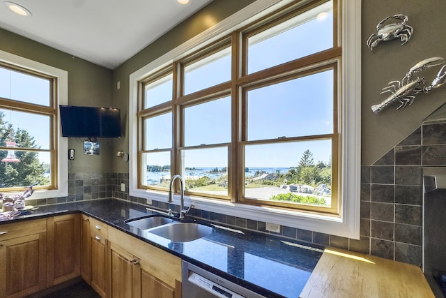kitchen with a sink, dishwasher, brown cabinets, decorative backsplash, and dark stone counters