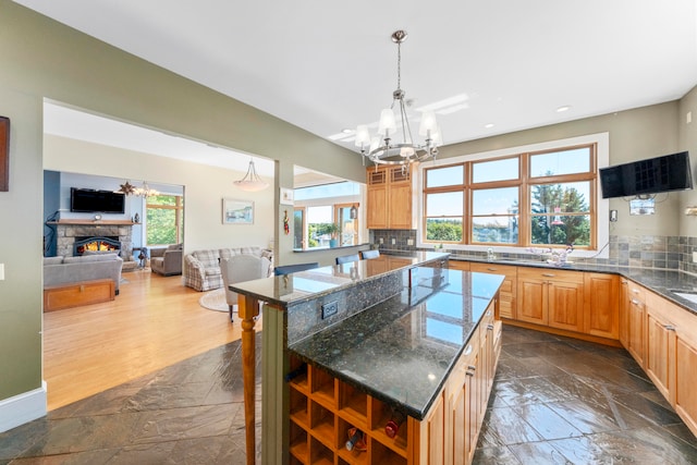 kitchen with a fireplace, dark stone countertops, tasteful backsplash, a kitchen island, and an inviting chandelier