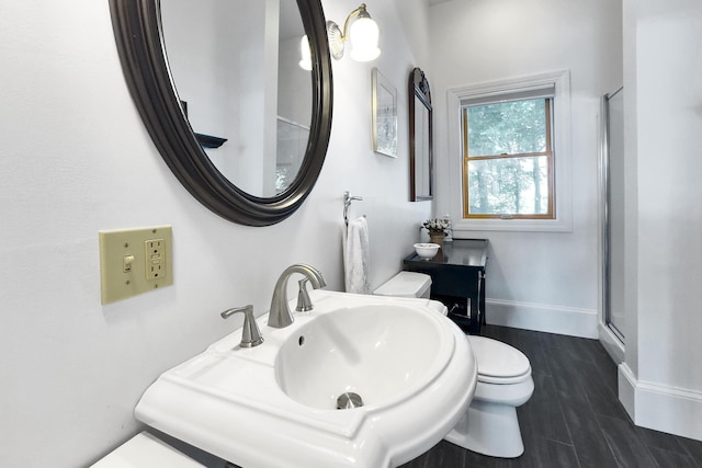 bathroom featuring toilet, a sink, a shower stall, wood finished floors, and baseboards