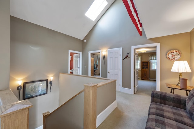 hallway featuring high vaulted ceiling, an upstairs landing, a skylight, baseboards, and light colored carpet