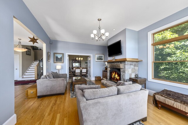 living room with stairs, light wood-style floors, a notable chandelier, and a stone fireplace