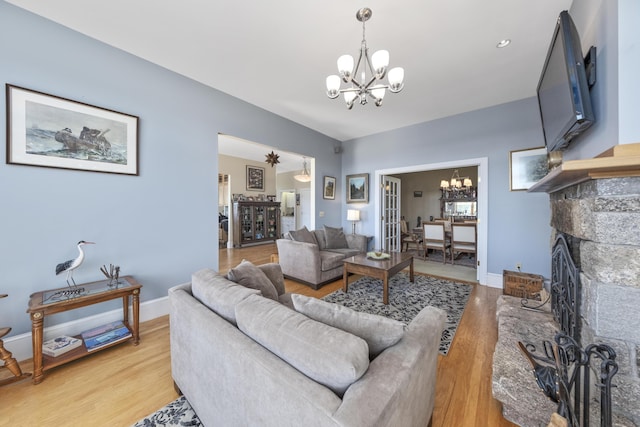 living room with an inviting chandelier, a stone fireplace, baseboards, and light wood-style floors