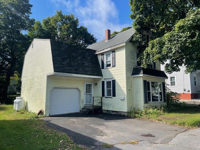 view of front of house featuring a garage, driveway, a chimney, and a gambrel roof