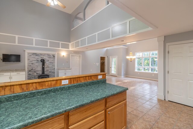 kitchen featuring light tile patterned floors, a wood stove, a high ceiling, and ceiling fan with notable chandelier