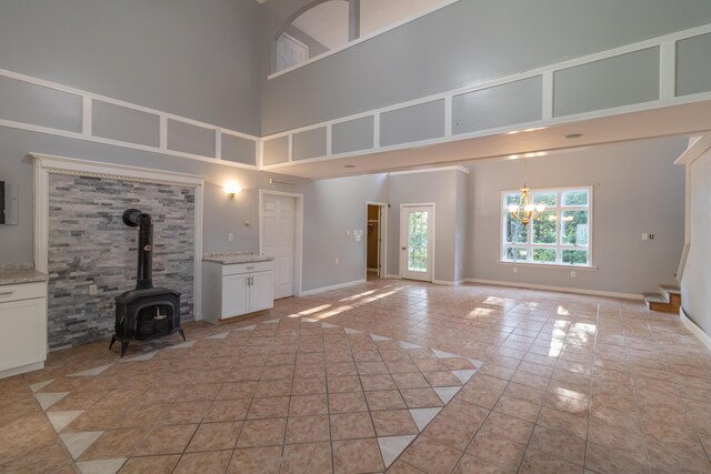 unfurnished living room with an inviting chandelier, a wood stove, a high ceiling, and light tile patterned floors