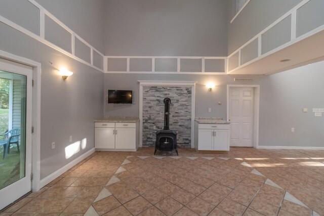 unfurnished living room with a towering ceiling, light tile patterned floors, and a wood stove