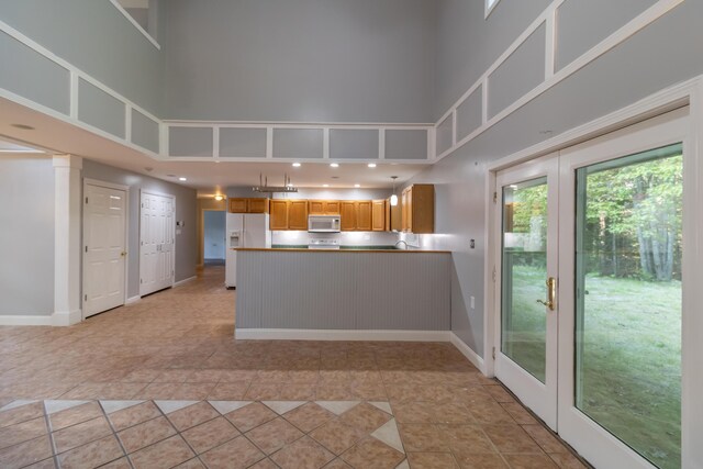 kitchen with white appliances, a towering ceiling, kitchen peninsula, and french doors