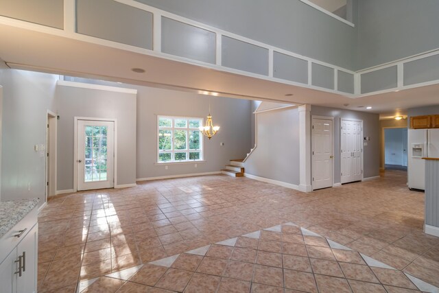 unfurnished living room with a notable chandelier, a towering ceiling, and light tile patterned floors