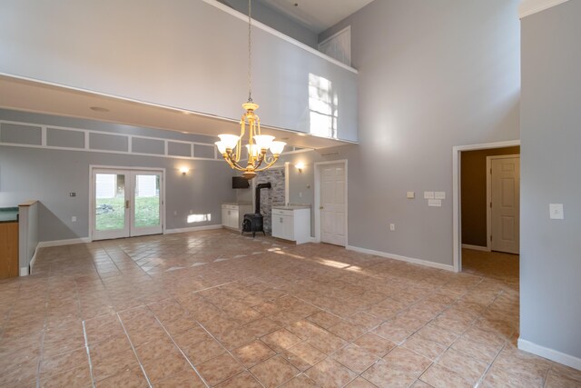 unfurnished living room with an inviting chandelier, a wood stove, light tile patterned flooring, and a high ceiling